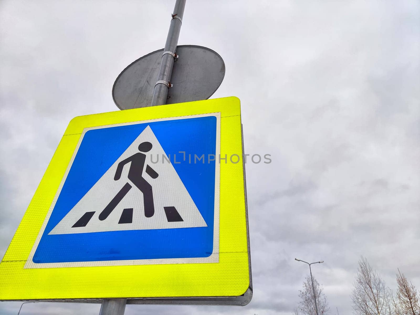 A pedestrian crossing sign on the background of a gray sky with clouds. Drawing, pictogram for pedestrians crossing the road