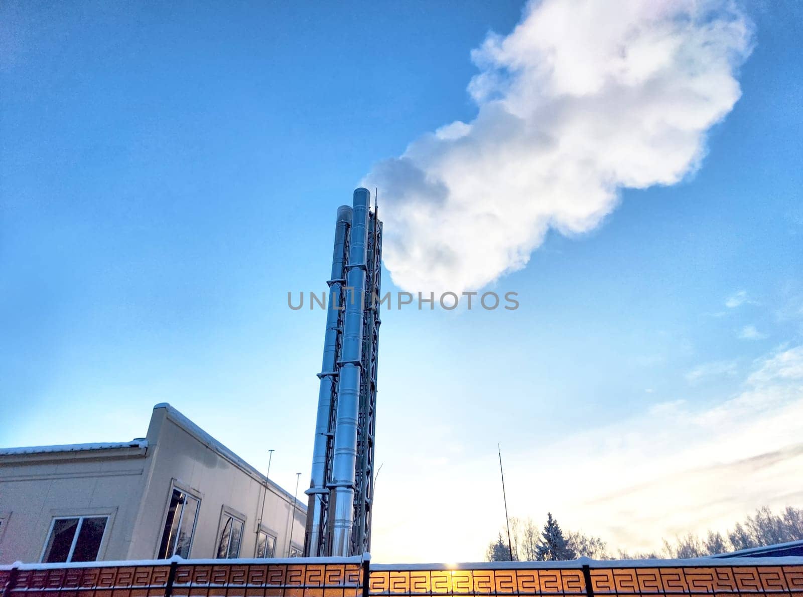 Air pollution by smoke coming out of two factory chimneys. White clouds of smoke against a blue sky background
