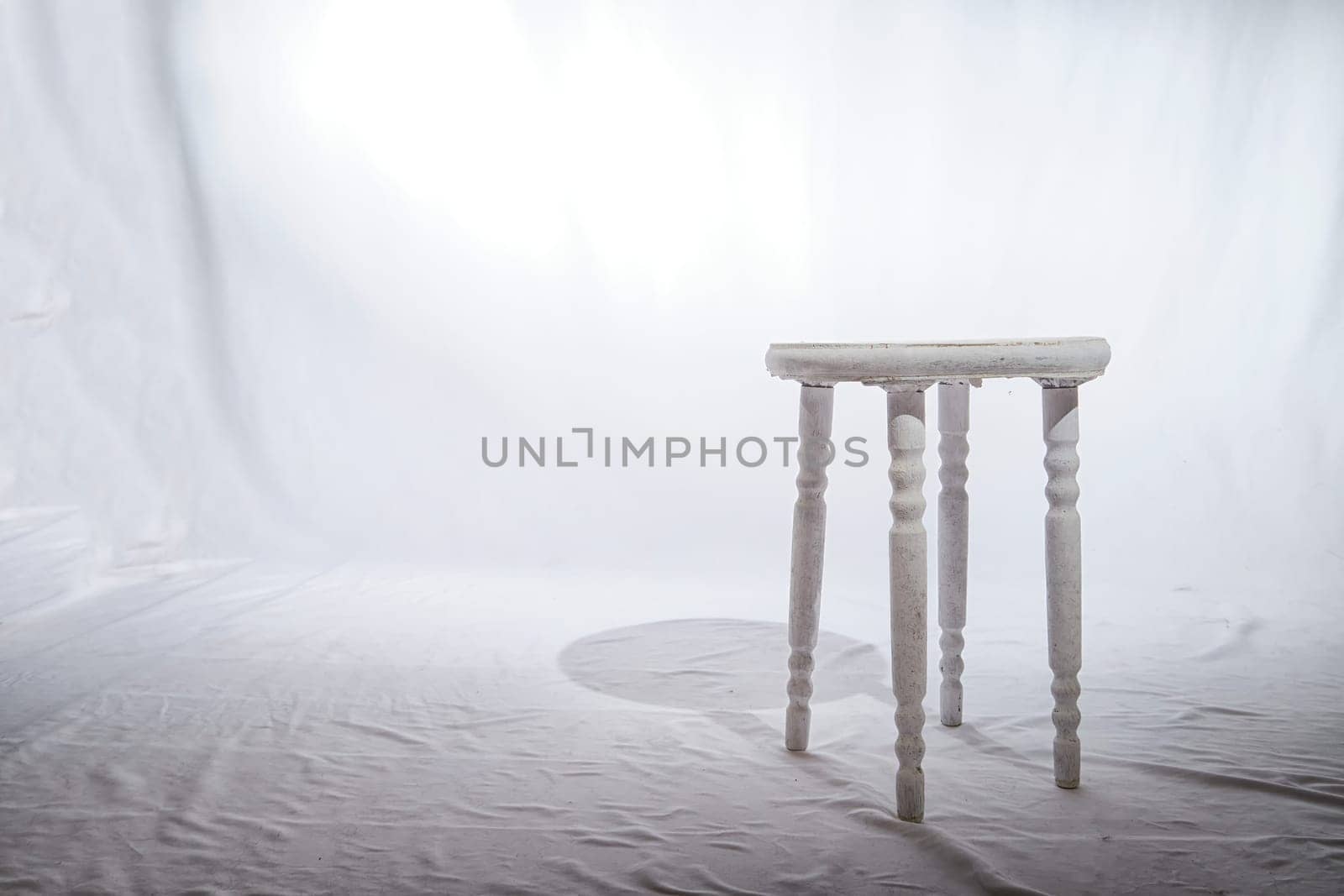 Solitary Wooden Stool in a White Minimalist Setting. Lone, white-painted wooden stool stands centered on textured surface, surrounded by soft white backdrop