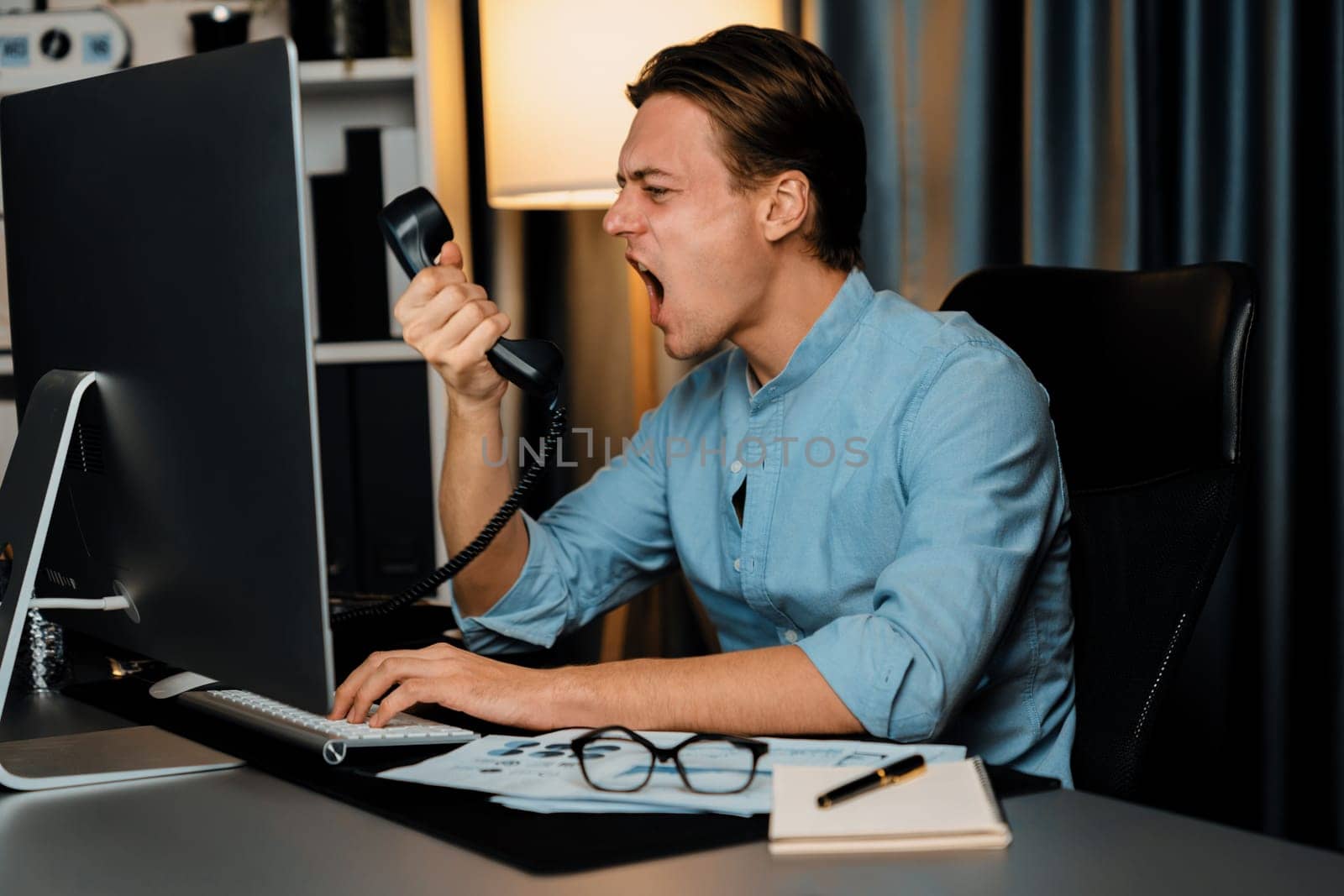Smart businessman calling with telephone office argument shouting over talking with partners on dynamic data marketing analysis plan surrounded paper on pc monitor at home office at night. Pecuniary.