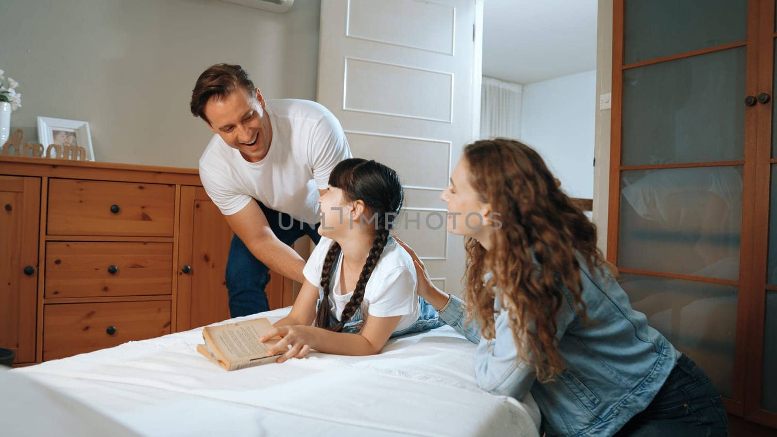 Bedtime story with childhood storytelling, mom and dad reading a fantasy book together to their little young girl in cozy and comfortable bedroom. Modern family happy time. Synchronos