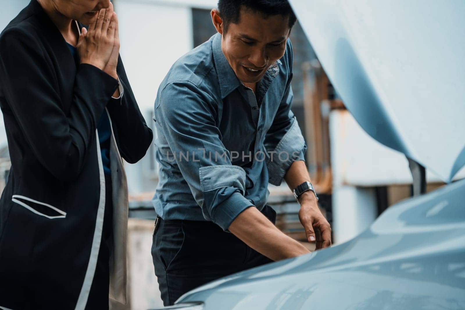 Man help woman fix the car problem. He pop up the car hood to repair the damaged part. uds