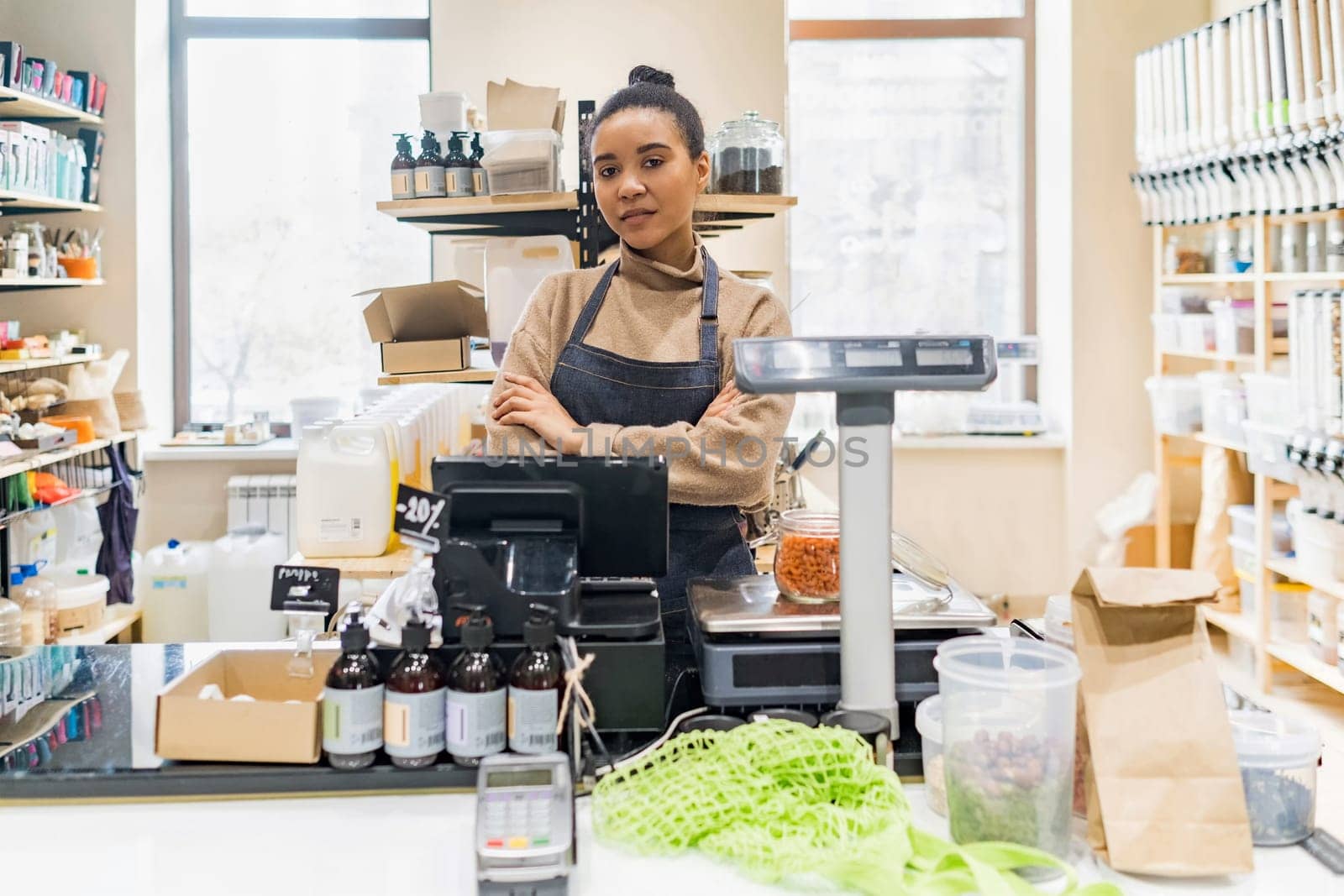 Portrait of confident African American woman owner of local zero waste grocery store wearing apron at cash desk