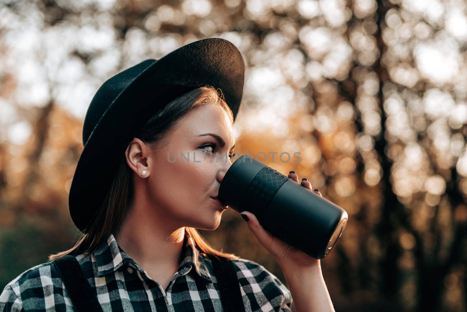 Hipster woman drinking hot coffee or tea, thermos, golden park, forest in autumn by kristina_kokhanova