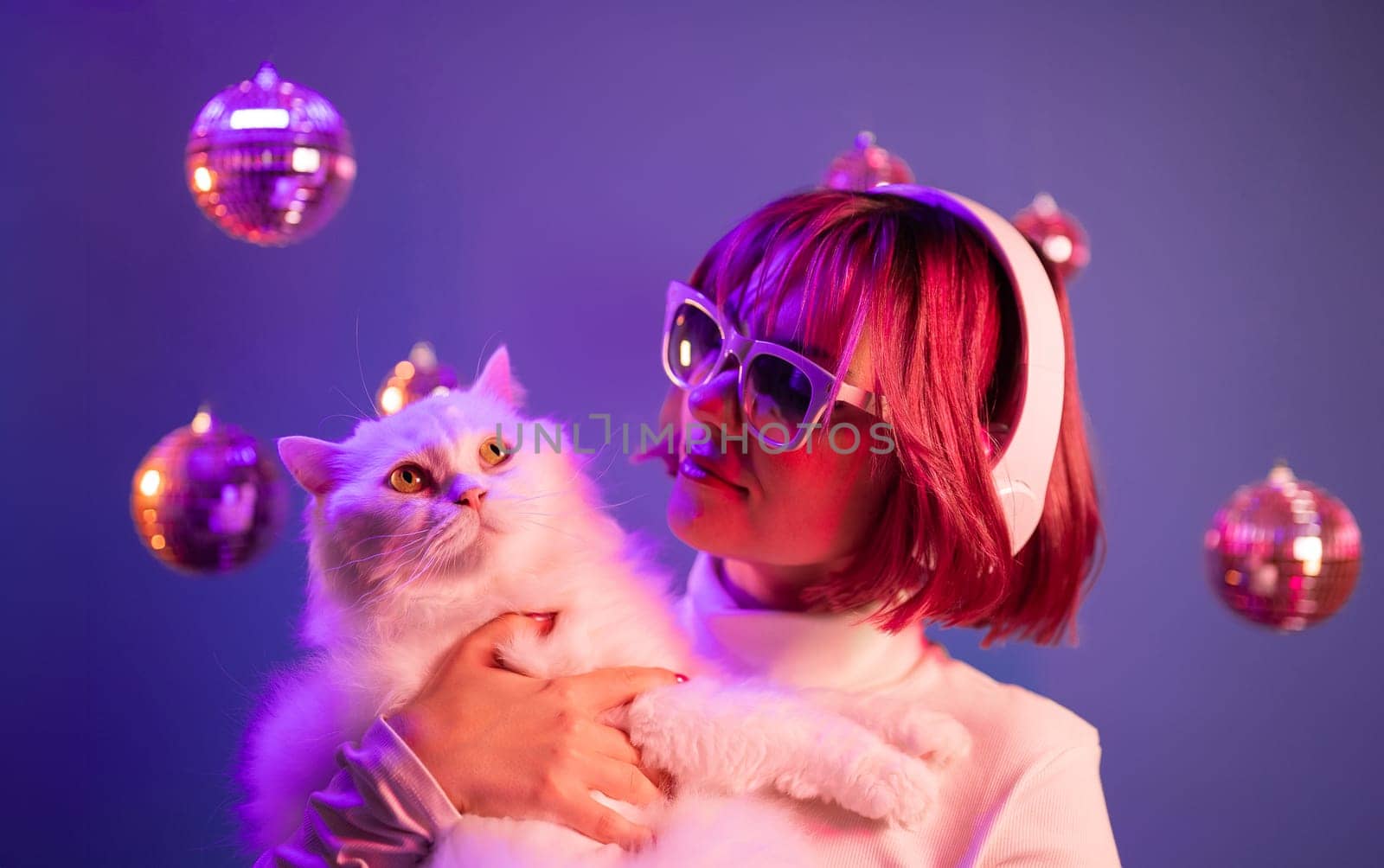 Disco woman with cat in fashion glasses listening music, dancing with headphones in colorful studio. Party, radio, headset concept.