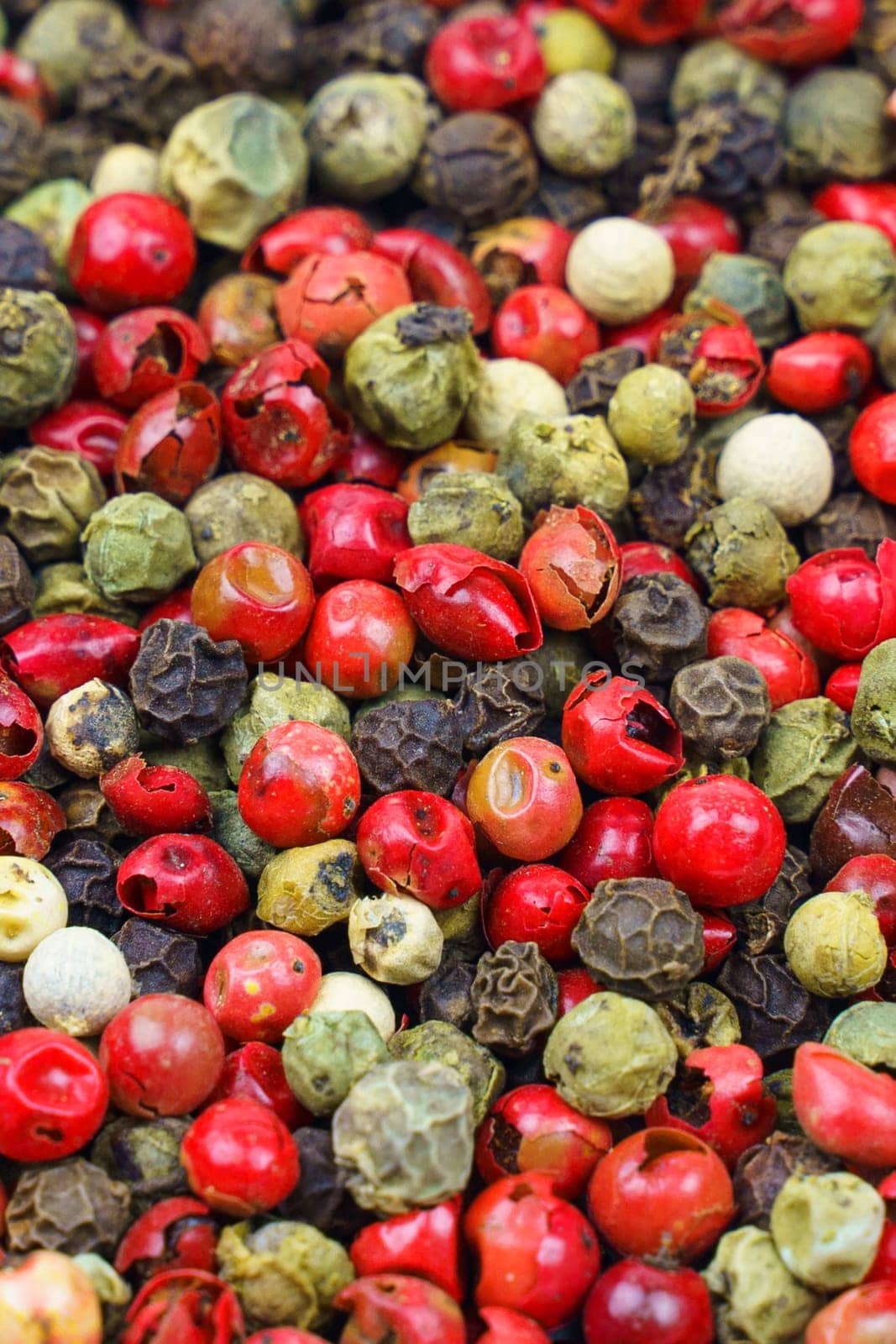 Background image. Top view of a mix of red, green, black, gray and white peppercorns. Vertical frame.