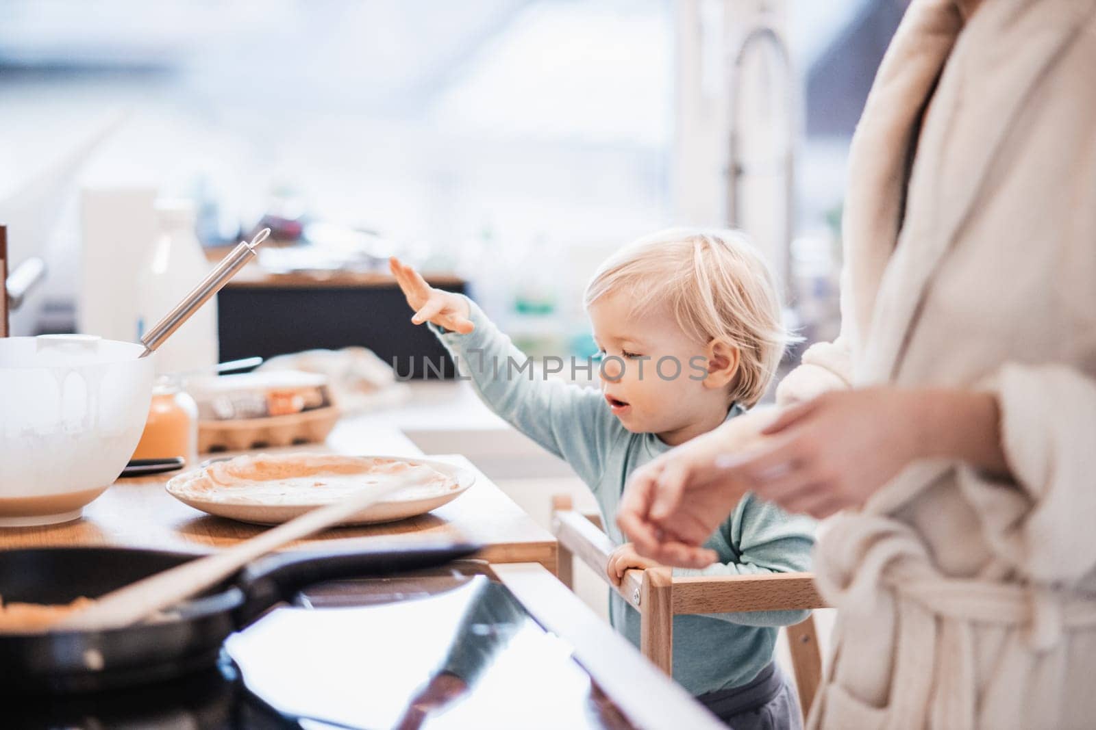 Mother and little toddler baby boy making pancakes for breakfast together in domestic kitchen. Family, lifestyle, domestic life, food, healthy eating and people concept
