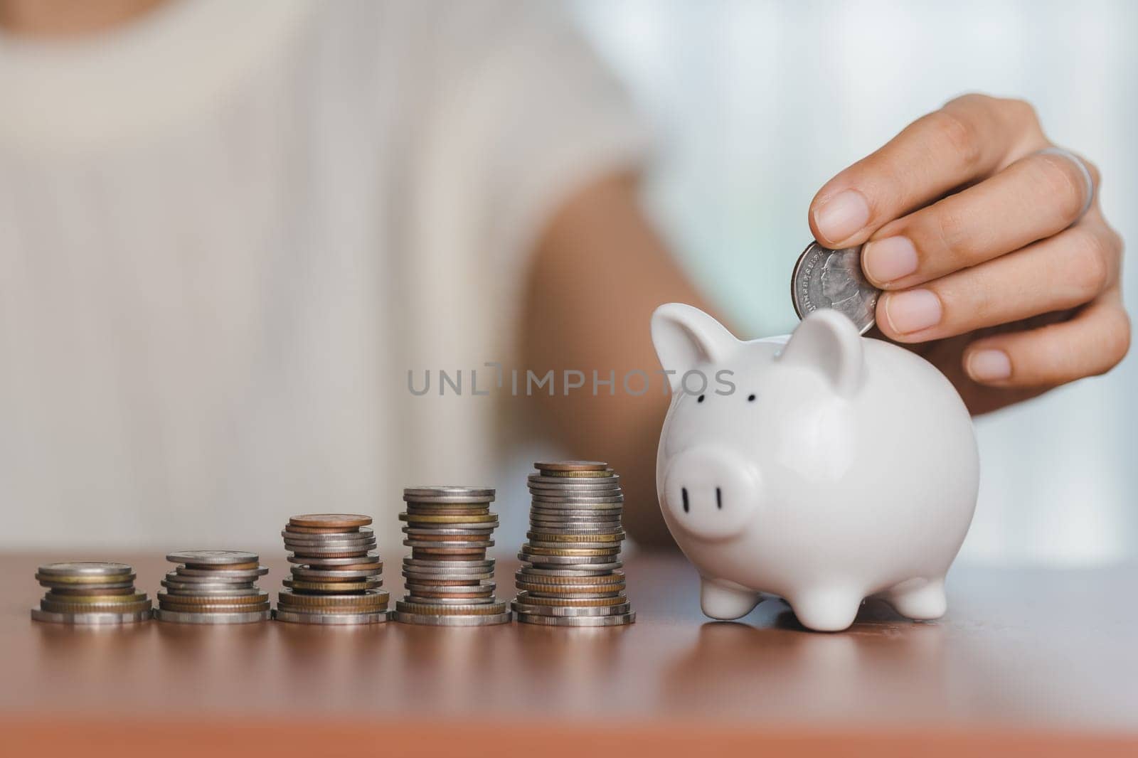 Hand saving money into a piggy bank with coins for savings, finance, and wealth in a business and banking concept