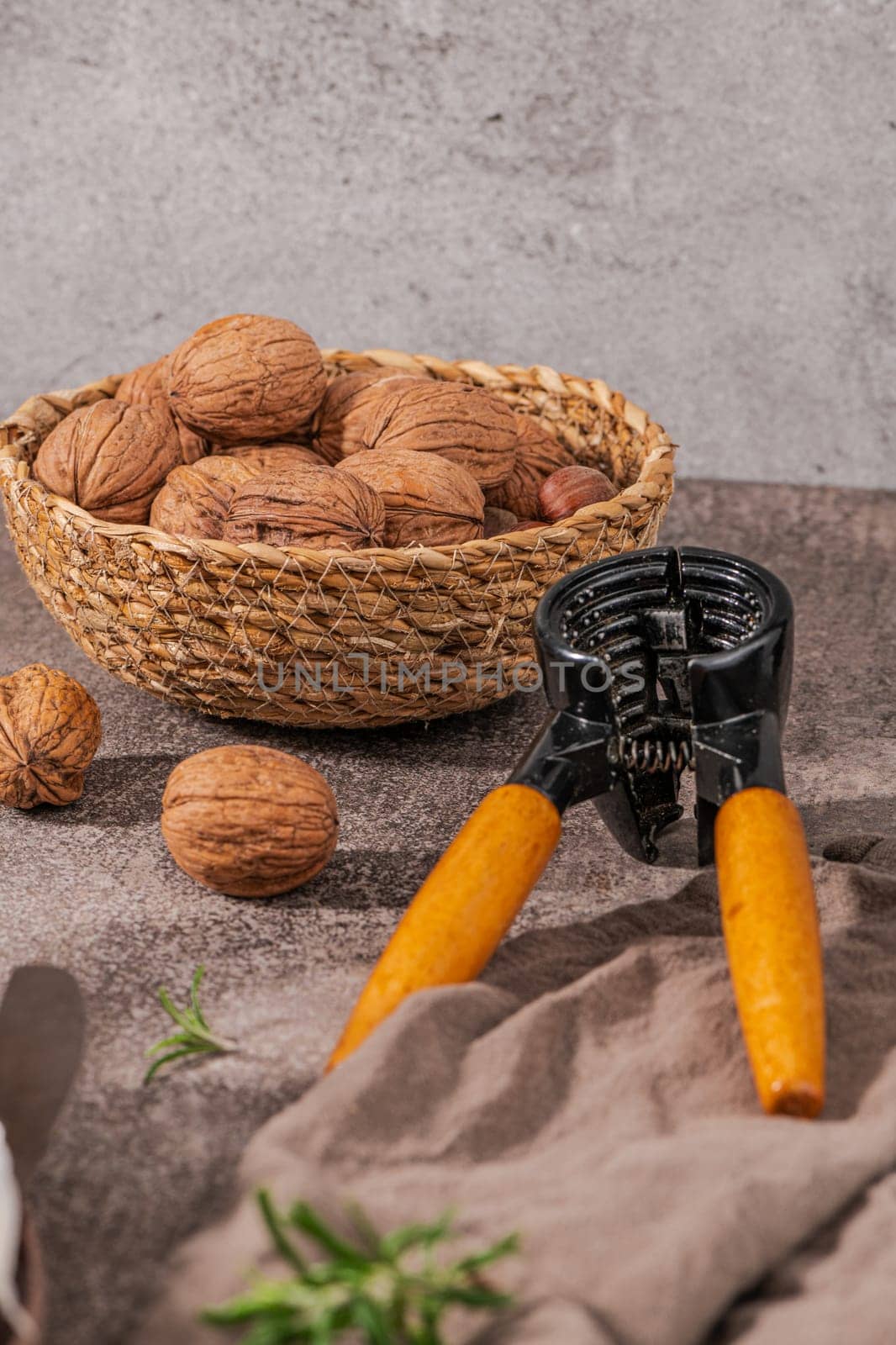 Basket with walnuts and hazelnuts and a nut cracker on a rustic kitchen counter.