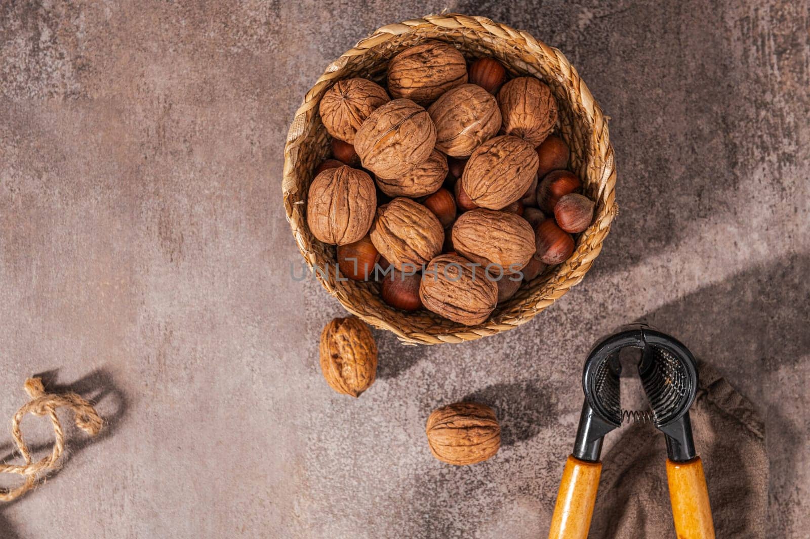 Basket with walnuts and hazelnuts and a nut cracker on a rustic kitchen counter.