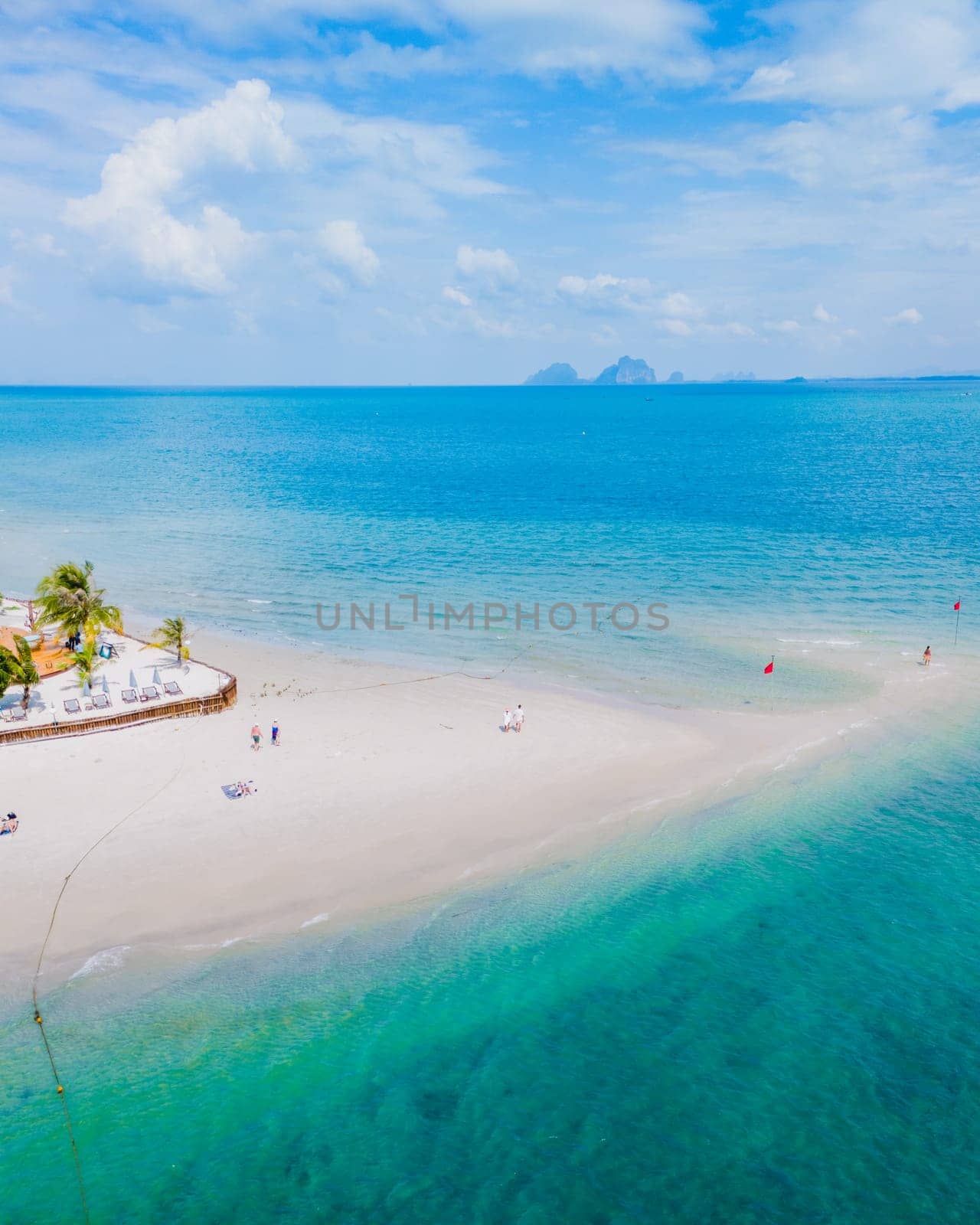 couple at a sandbar in the ocean of Koh Muk a tropical island with palm trees and soft white sand, and a turqouse colored ocean in Koh Mook Trang Thailand on a sunny day with blue sky
