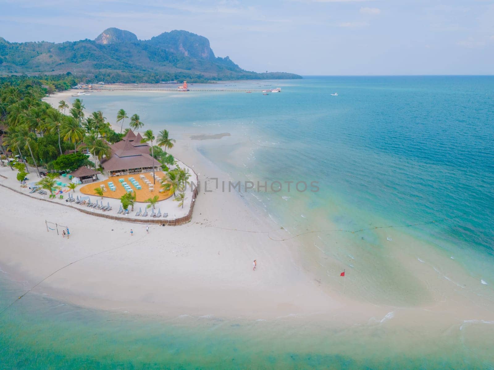 couple at a sandbar in the ocean of Koh Muk a tropical island with palm trees and soft white sand, and a turqouse colored ocean in Koh Mook Trang Thailand on a sunny day with blue sky