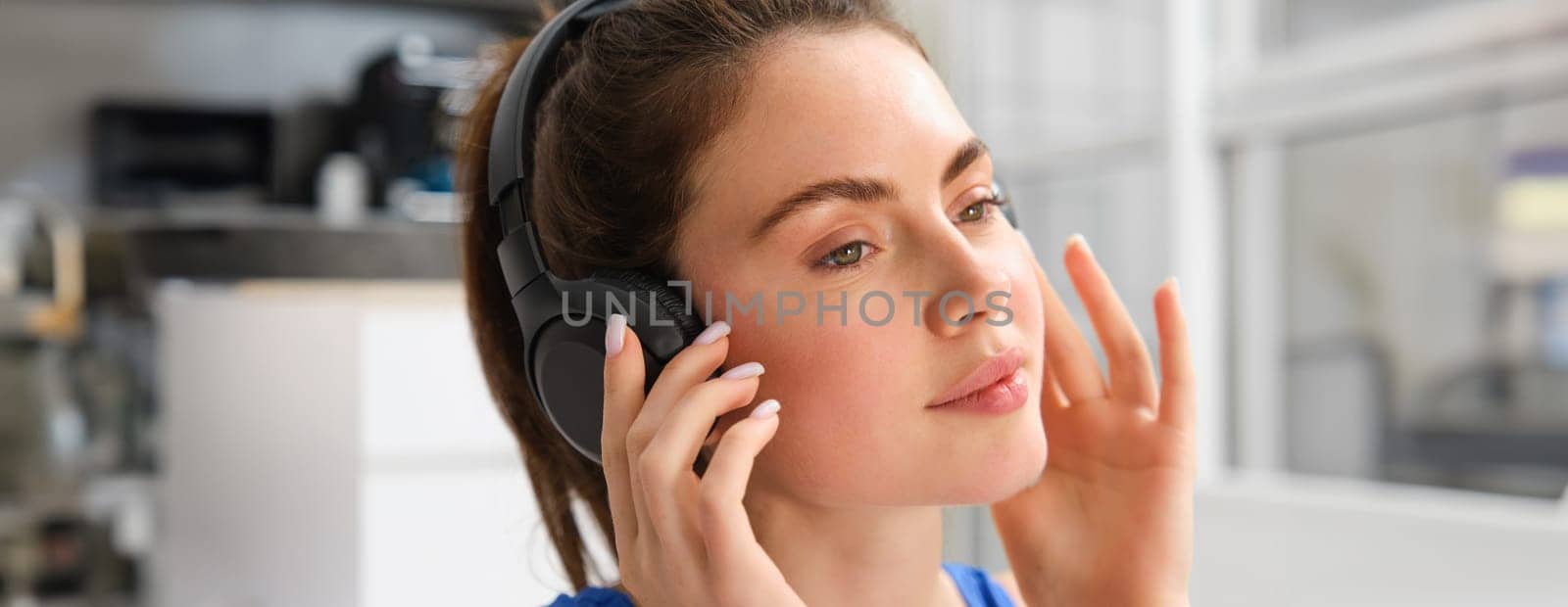 Close up portrait of fitness woman, smiling and listening music, wearing wireless black headphones.