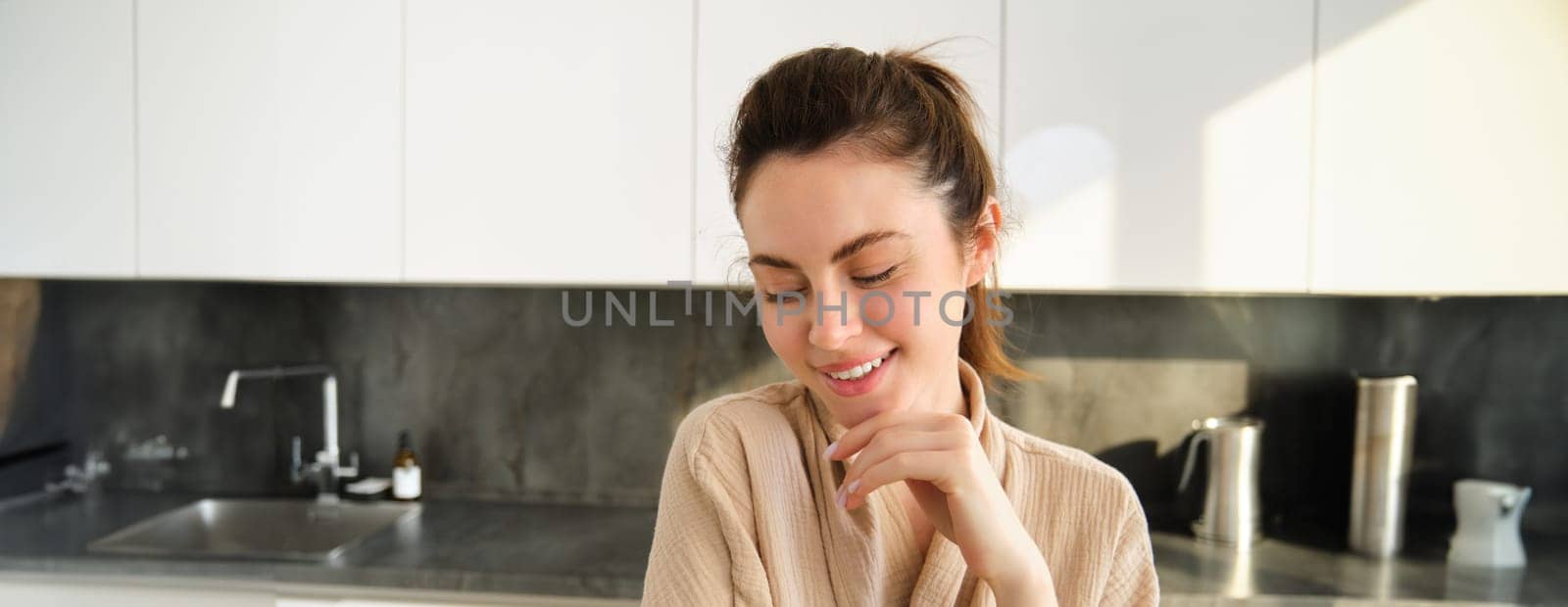 Portrait of beautiful young woman in bathrobe, cooking food, posing in kitchen and making dinner, preparing meal, smiling happy at camera, eating healthy. Copy space