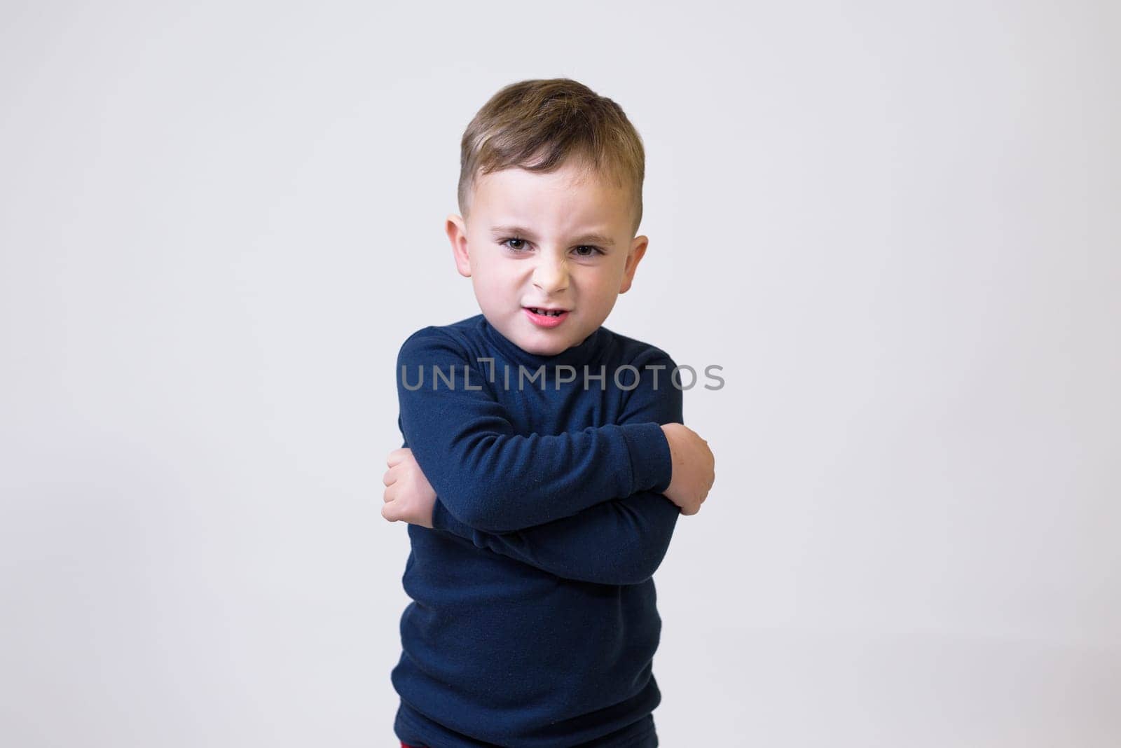 Portrait of an upset cute little kid standing with arms folded and looking at camera isolated over white background by jcdiazhidalgo