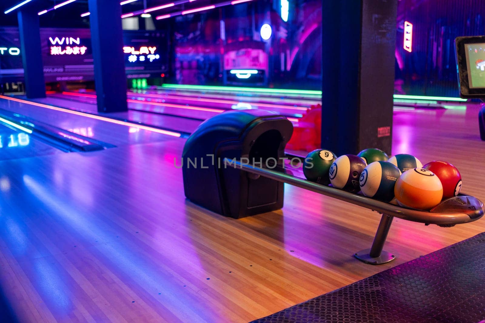 Modern bowling interior with ball rack and vibrant red and blue lighting along the alleys, creating an atmosphere of amusement and fun.