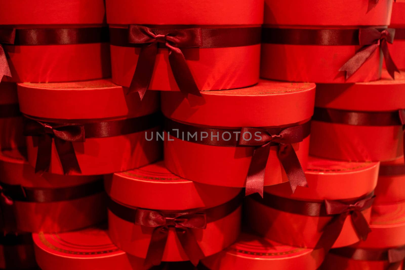 Closeup of gift boxes tied with ribbons, illuminated with warm red light. Stack of presents displayed for sale at retail store, conveying festive and inviting atmosphere.