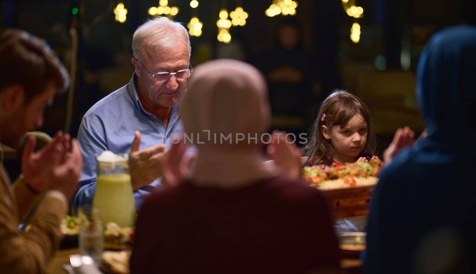 In a modern restaurant setting, a European Islamic family comes together for iftar during Ramadan, engaging in prayer before the meal, uniting tradition and contemporary practices in a celebration of faith and family by dotshock