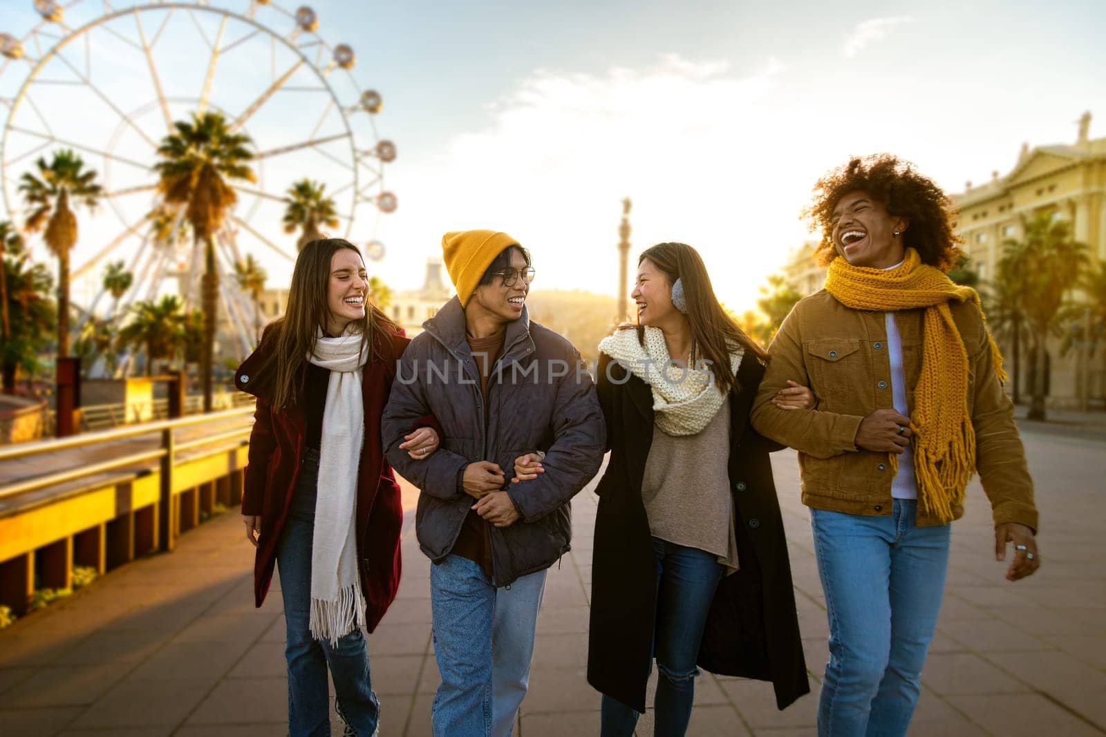 Front view of group of happy multiracial friends walking around city laughing and talking together while on a sunny winter day. College student and lifestyle concept.