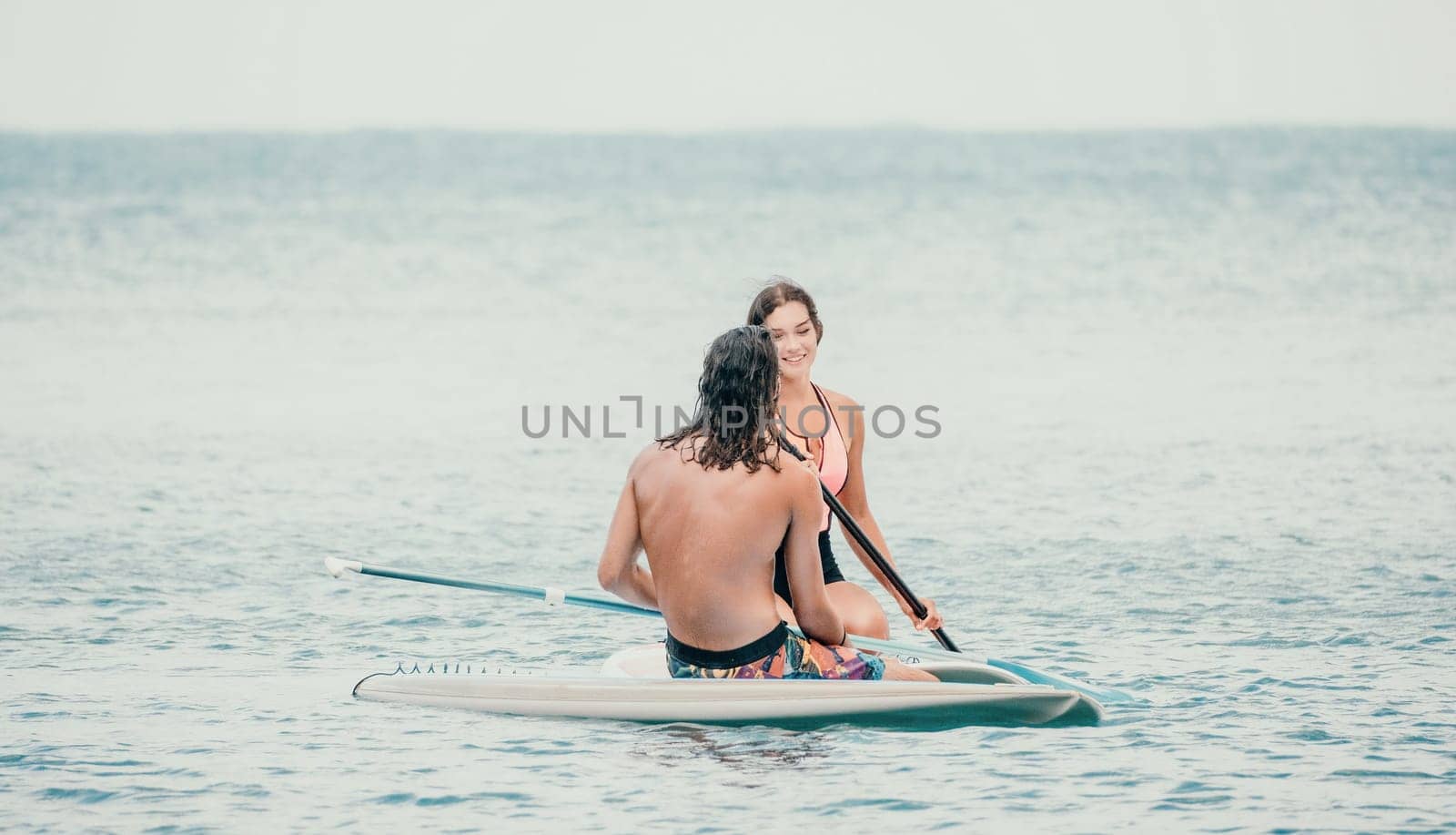 Sea woman and man on sup. Silhouette of happy young woman and man, surfing on SUP board, confident paddling through water surface. Idyllic sunset. Active lifestyle at sea or river