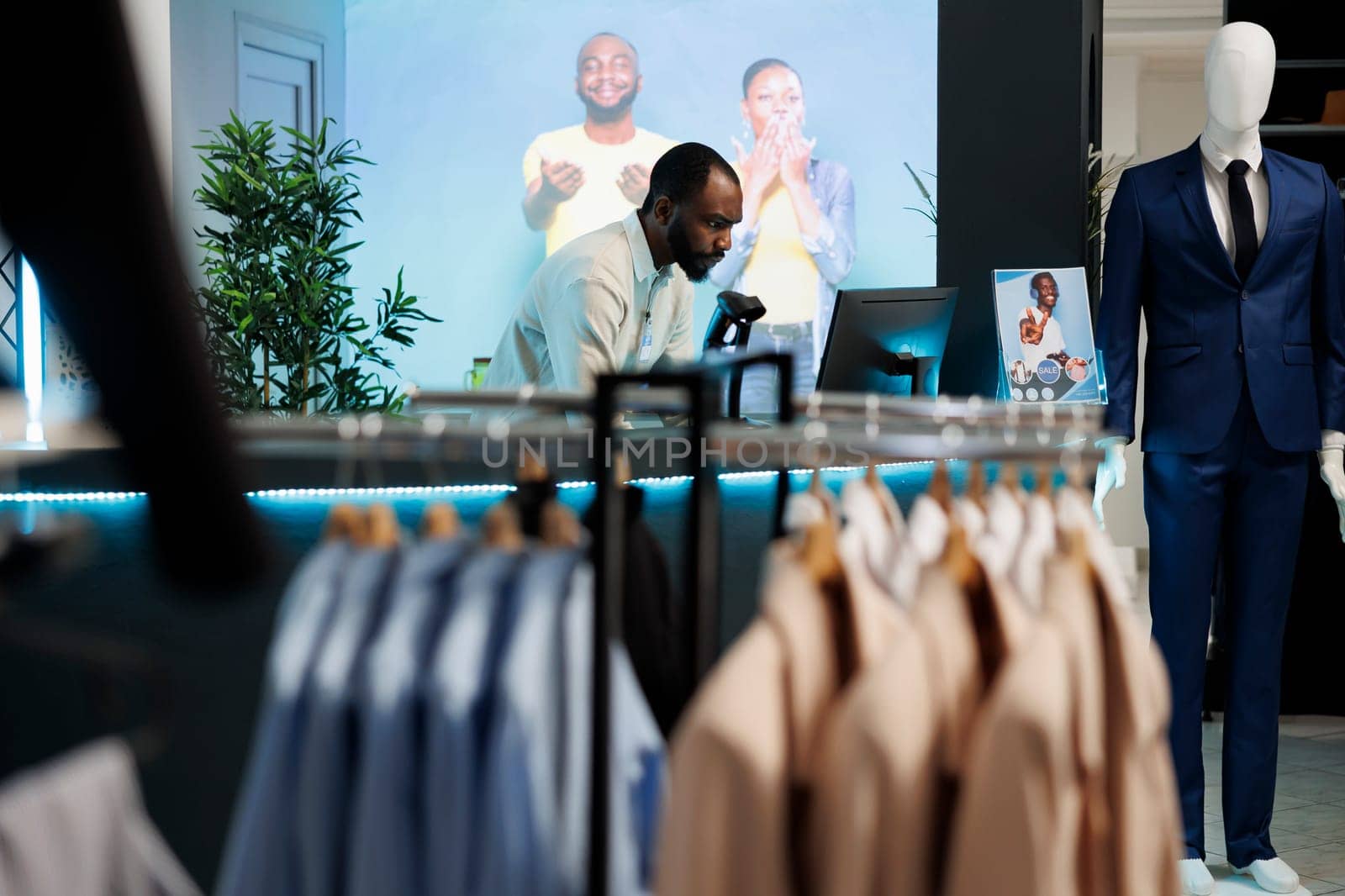 Man cashier working on computer at counter desk in trendy retail clothing store. Shopping mall boutique department african american assistant standing at checkout cash register