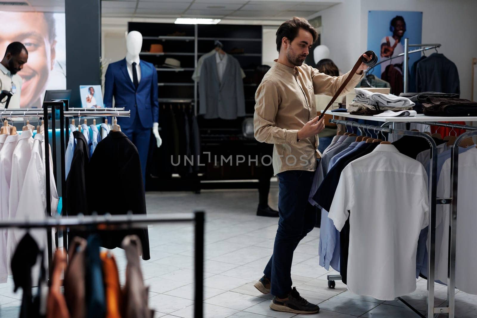 Caucasian man choosing leather belt and examining style while shopping in clothing store. Fashion boutique buyer selecting accessory and checking quality before making purchase