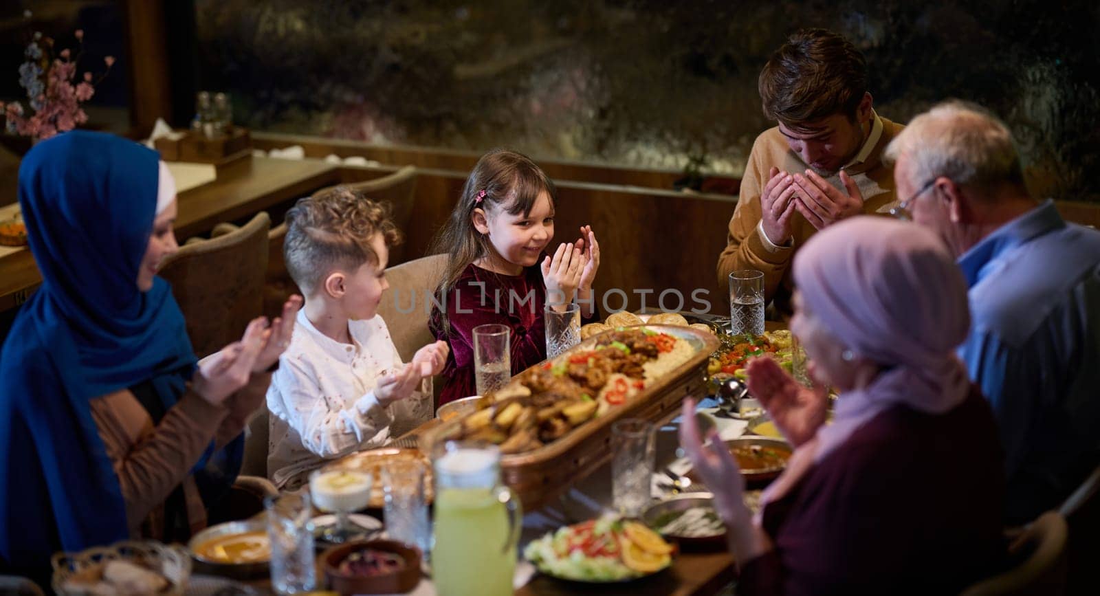 In a modern restaurant setting, a European Islamic family comes together for iftar during Ramadan, engaging in prayer before the meal, uniting tradition and contemporary practices in a celebration of faith and family by dotshock