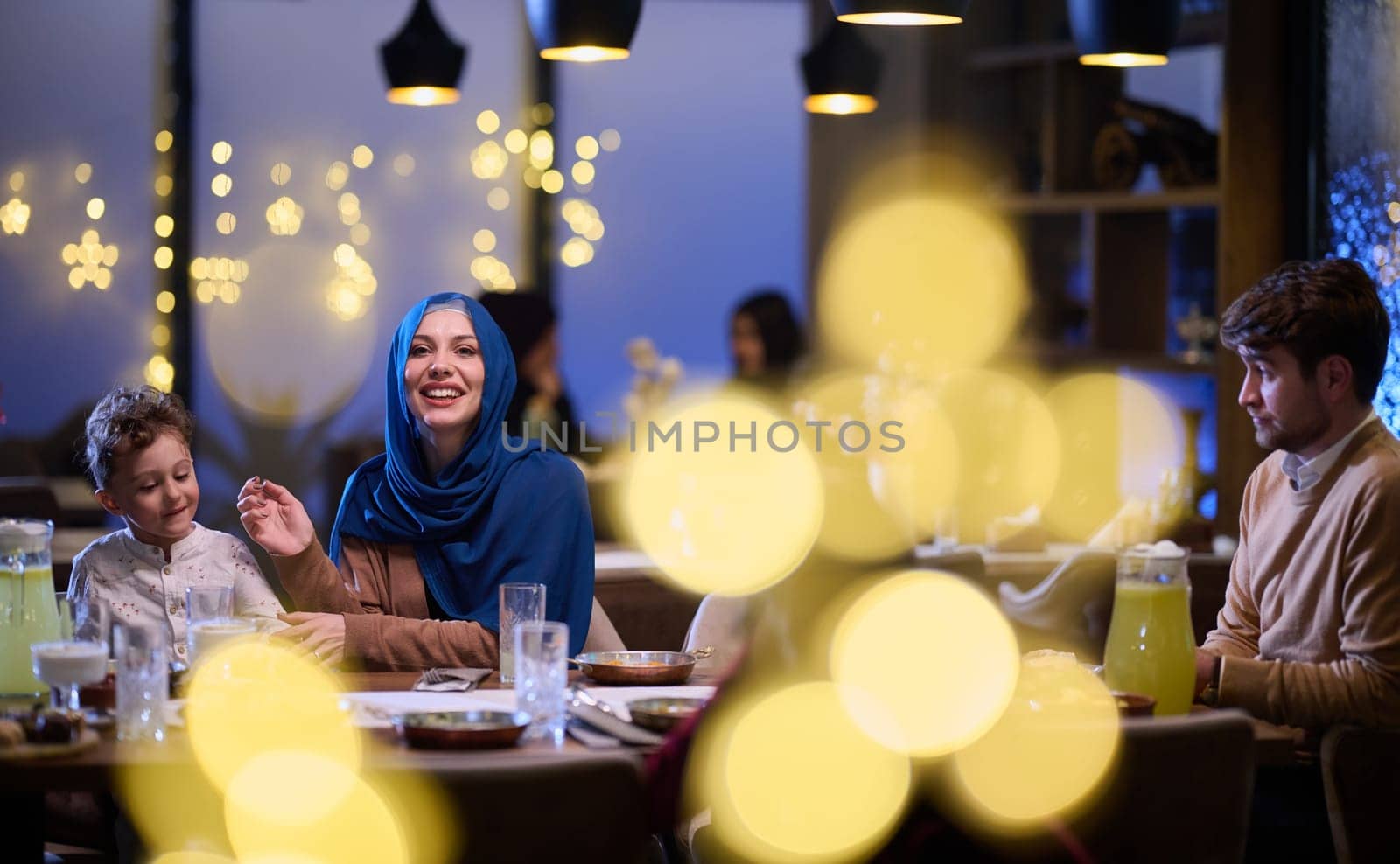 In a modern restaurant, an Islamic couple and their children joyfully await their iftar meal during the holy month of Ramadan, embodying familial harmony and cultural celebration amidst the contemporary dining ambiance by dotshock