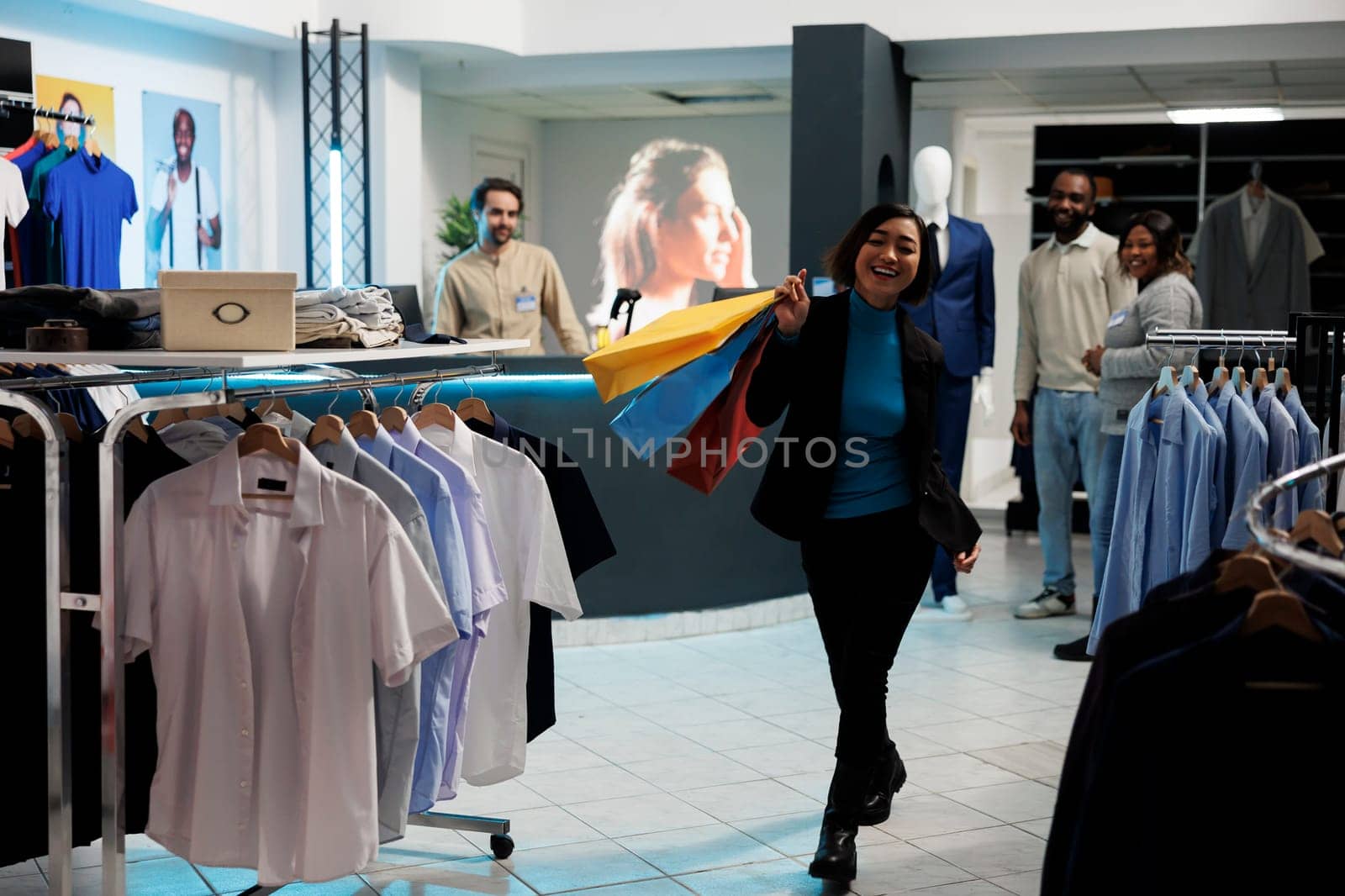 Clothing store satisfied customer walking with shopping bags in clothing store and looking at camera. Cheerful smiling asian woman carrying paper bags with trendy apparel purchase in mall