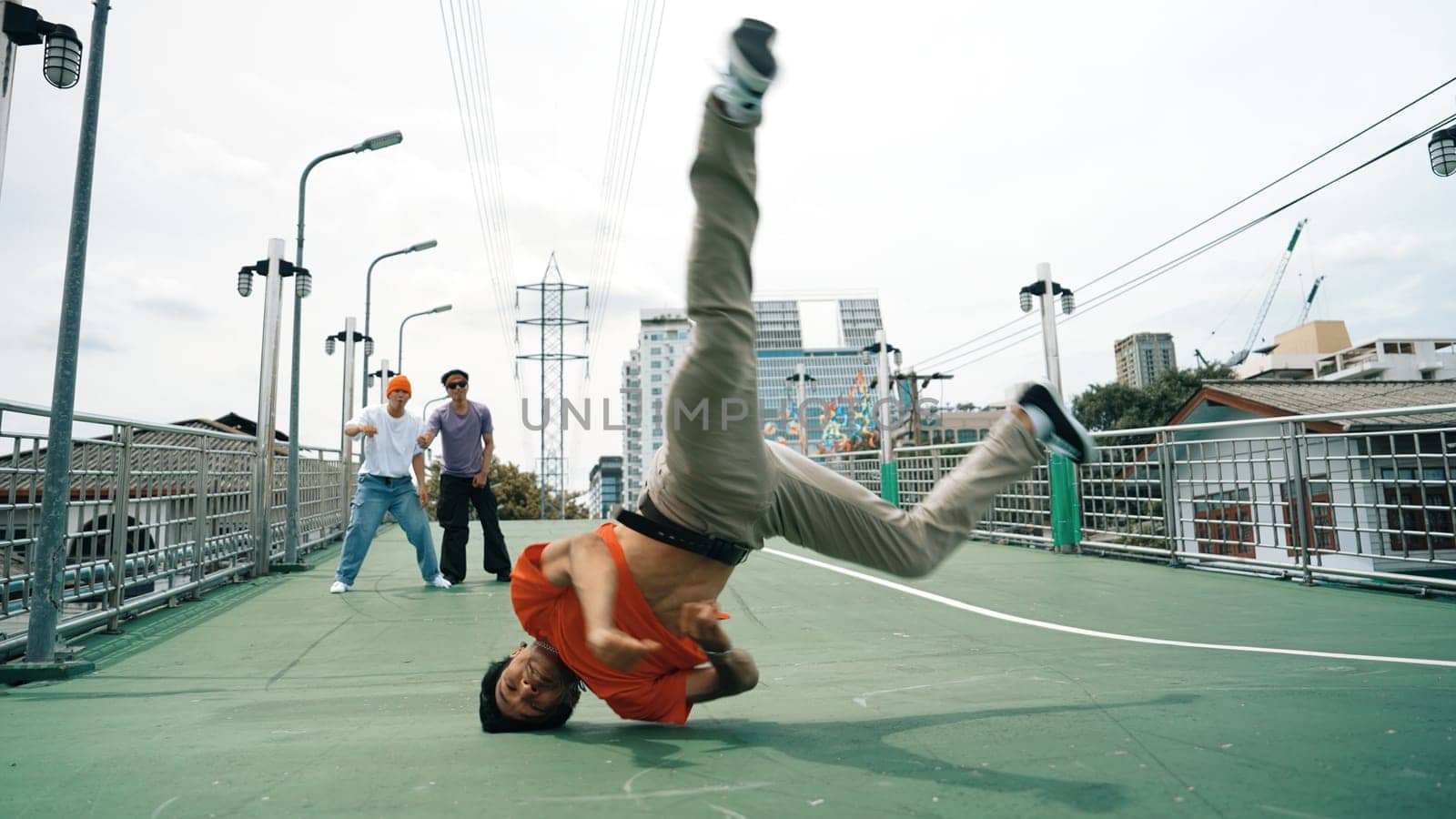 Young happy hipster perform break dancing or foot step with friend moving to hiphop music together. Skilled dancer doing freeze pose and waving hand. Modern lifestyle. Outdoor music 2024. Sprightly.