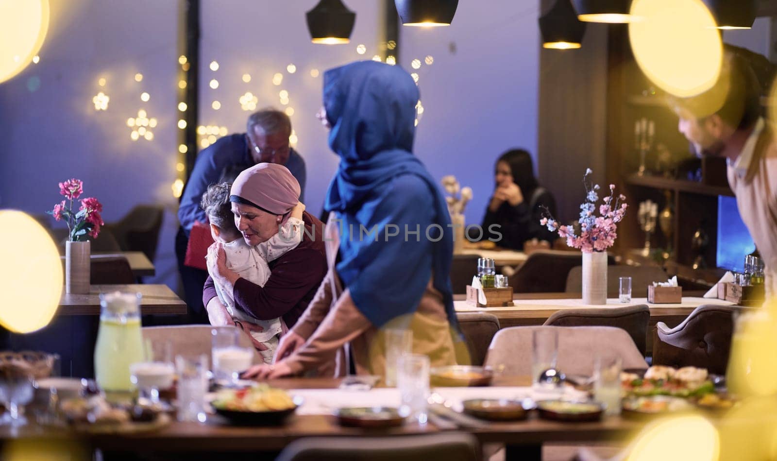 Grandparents arrive at their children's and grandchildren's gathering for iftar in a restaurant during the holy month of Ramadan, bearing gifts and sharing cherished moments of love, unity, and cultural exchange, as they eagerly await their meal together.