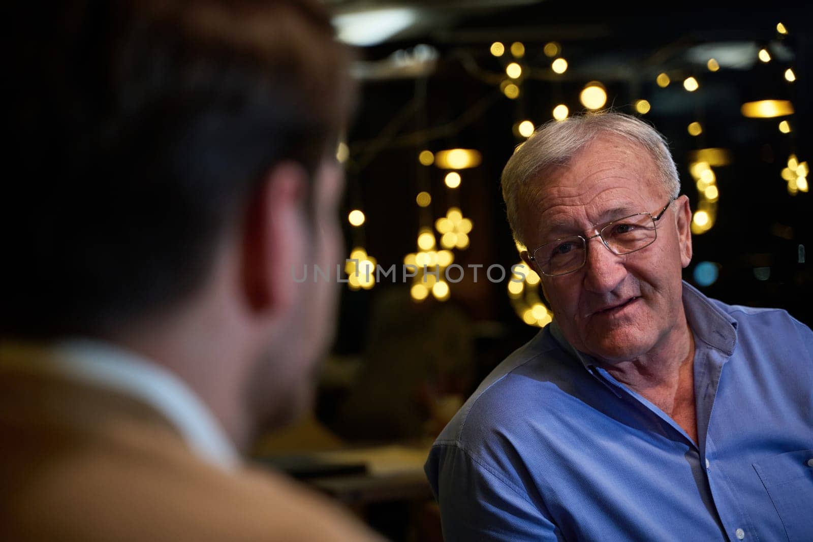 A son and his elderly father engage in heartfelt conversation while patiently awaiting their iftar meal, fostering intergenerational bonding and cherished moments of family connection.