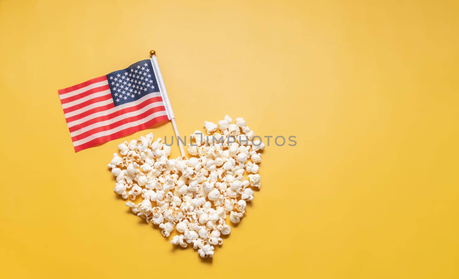 National Popcorn Lover's Day. Top View Popcorn in Heart Shape with American USA Flag on Yellow Background. Copy Space for Text. Greeting Card, Template No Text. Tasty salted Snack Flat Lay, Horizontal by netatsi