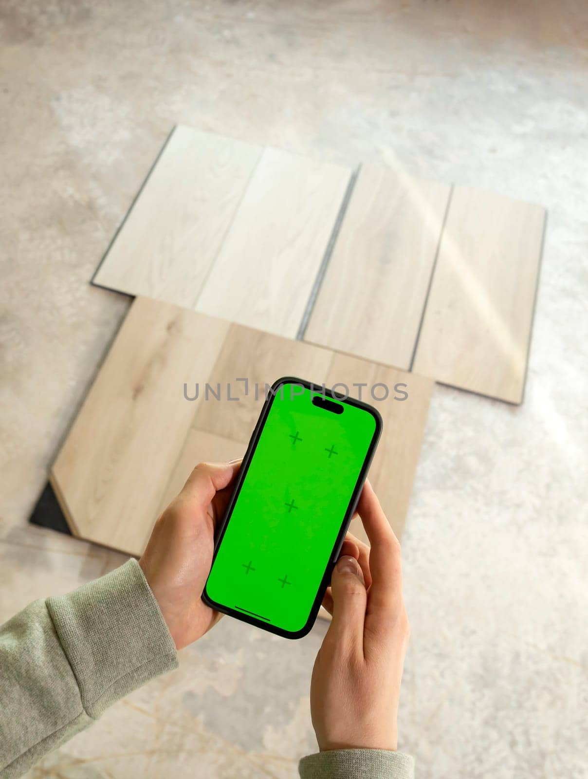 Hands Holding Device with Green Chroma Key Screen above Luxury Vinyl Wood Samples, Laminate On Floor In House. Choosing, Selecting Waterproof Flooring. Home Reconstruction. Vertical Plane.