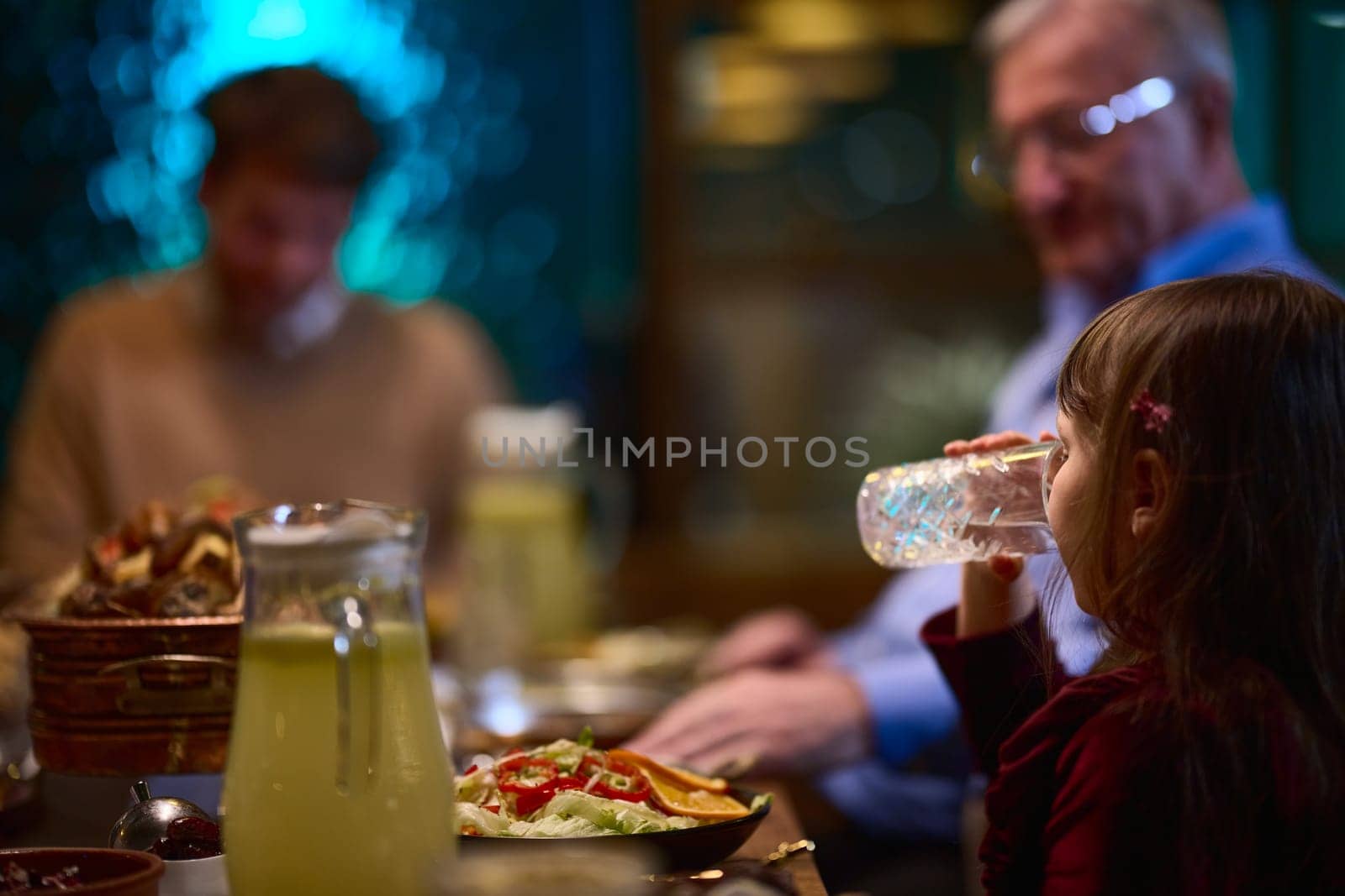 In a modern restaurant, a young girl participates in iftar by breaking her fast with water, embodying the tradition and significance of Ramadan in a contemporary setting. by dotshock