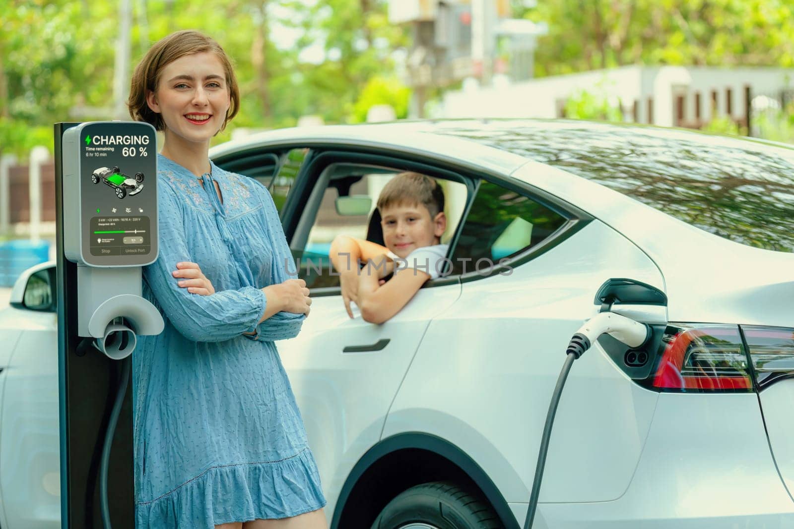 Environmental awareness family with eco-friendly electric car recharging battery from home EV charging station with little boy inside the car. Rechargeable and EV car technology. Perpetual