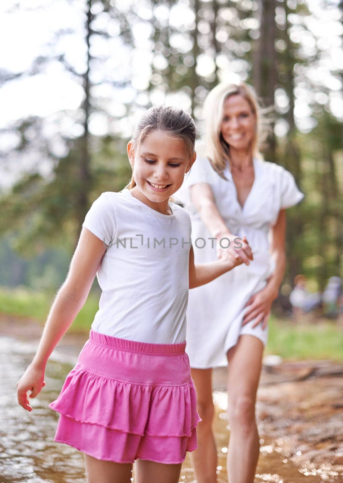 Mother, daughter and happiness outdoor in lake for bonding, support or holding hands on holiday in nature. Family, woman and girl child with smile or adventure on vacation, travel and river with love by YuriArcurs