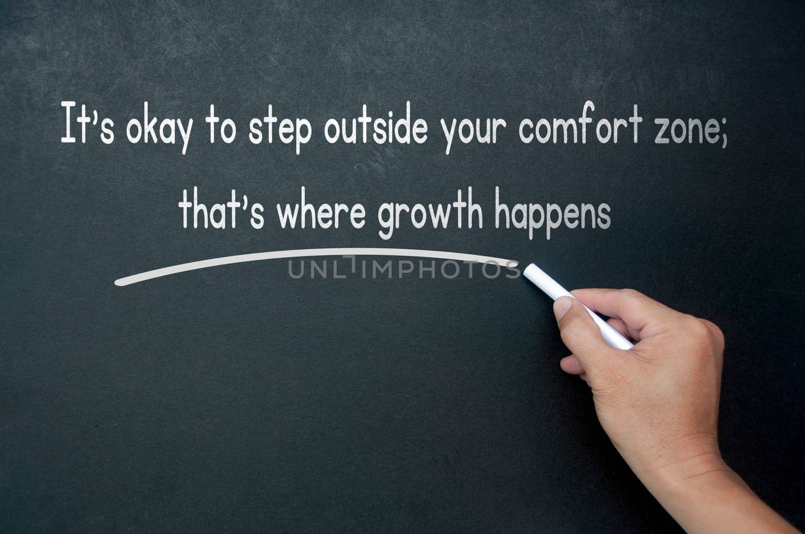 Hand writing It is okay to step outside your comfort zone affirmation on black board.