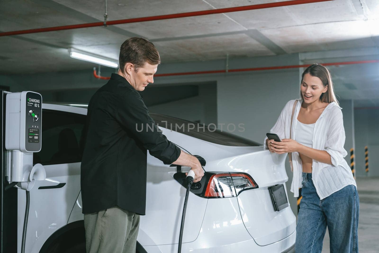 Young couple travel with EV electric car to shopping center parking lot charging in downtown city showing urban sustainability lifestyle by green clean rechargeable energy of electric vehicle innards