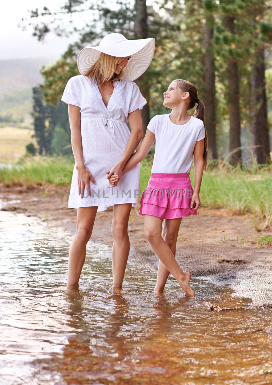 Mother, daughter and happiness outdoor in lake for bonding, support or holding hands on holiday in nature. Family, woman and girl child with smile or adventure on vacation, travel and river with love by YuriArcurs