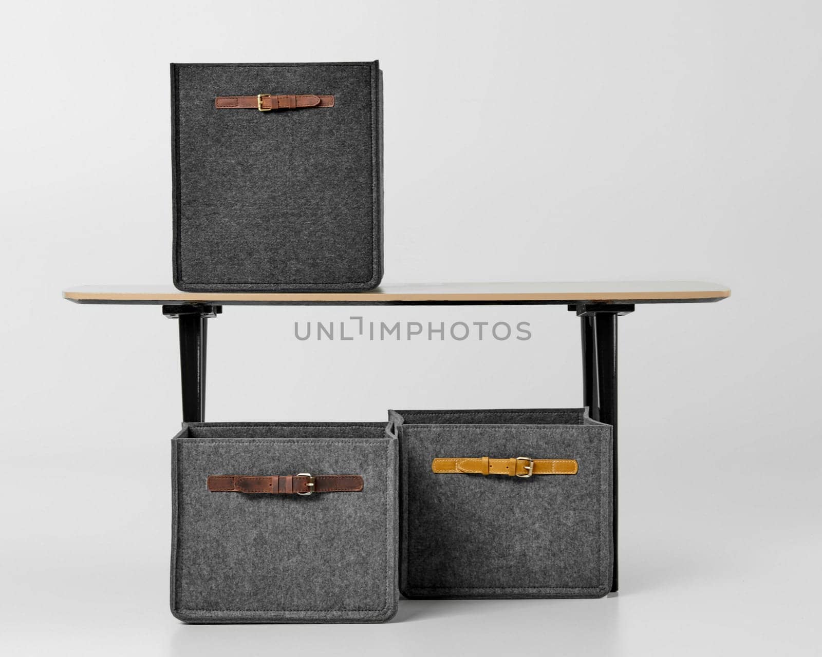 Handcrafted grey felt boxes with applied leather handles arranged by simple desk. Stylish accessory for organizing office space and storing stationery and documents