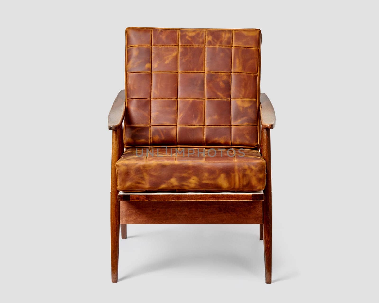 Vintage-inspired wooden chair with brown patchwork leather upholstery and distinctive armrests, against light backdrop. Stylish piece of furniture for cozy interior