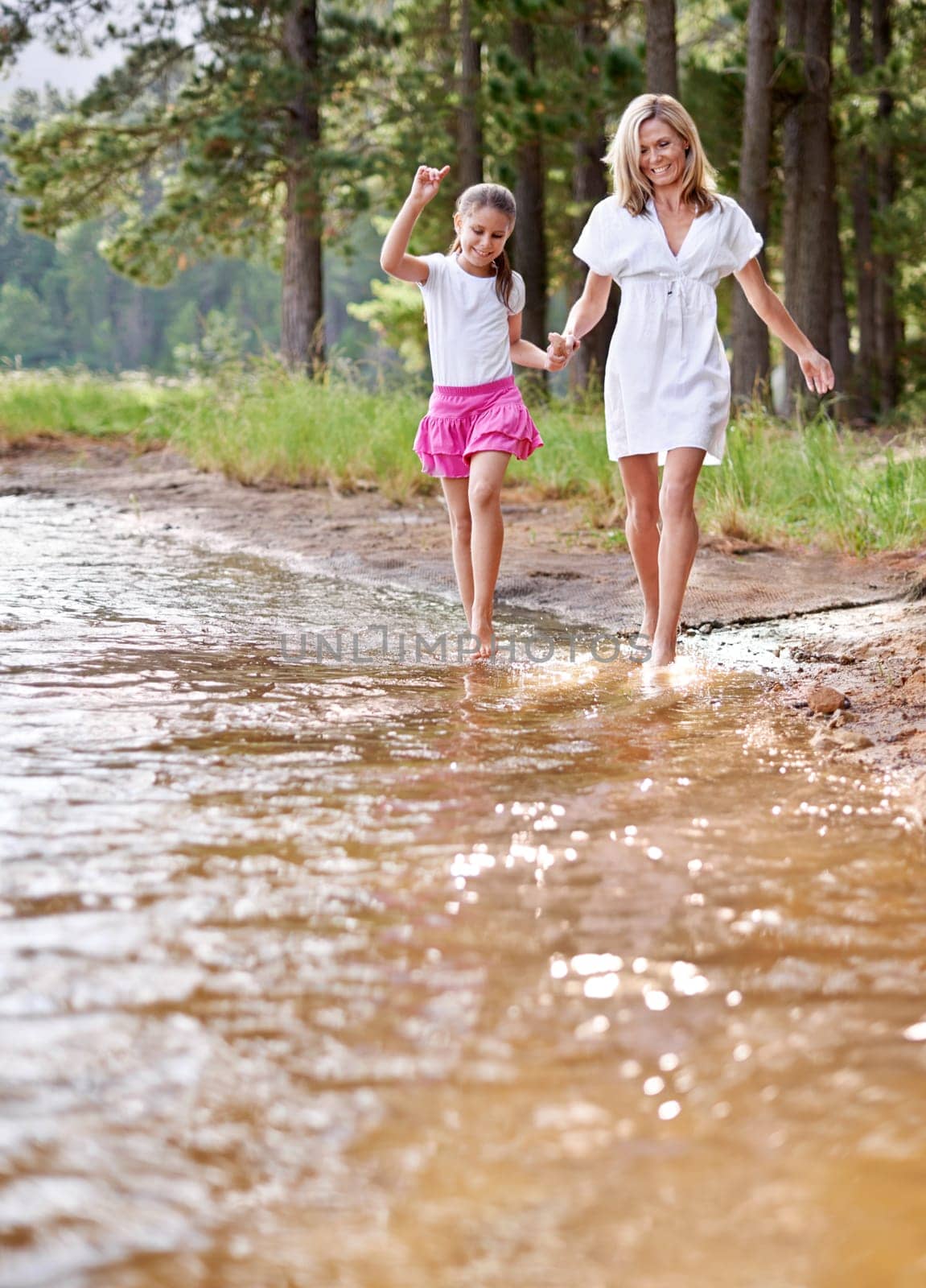 Mother, daughter and happiness outdoor in river for bonding, support or holding hands on holiday in nature. Family, woman and girl child with smile or adventure on vacation, travel and lake with love by YuriArcurs