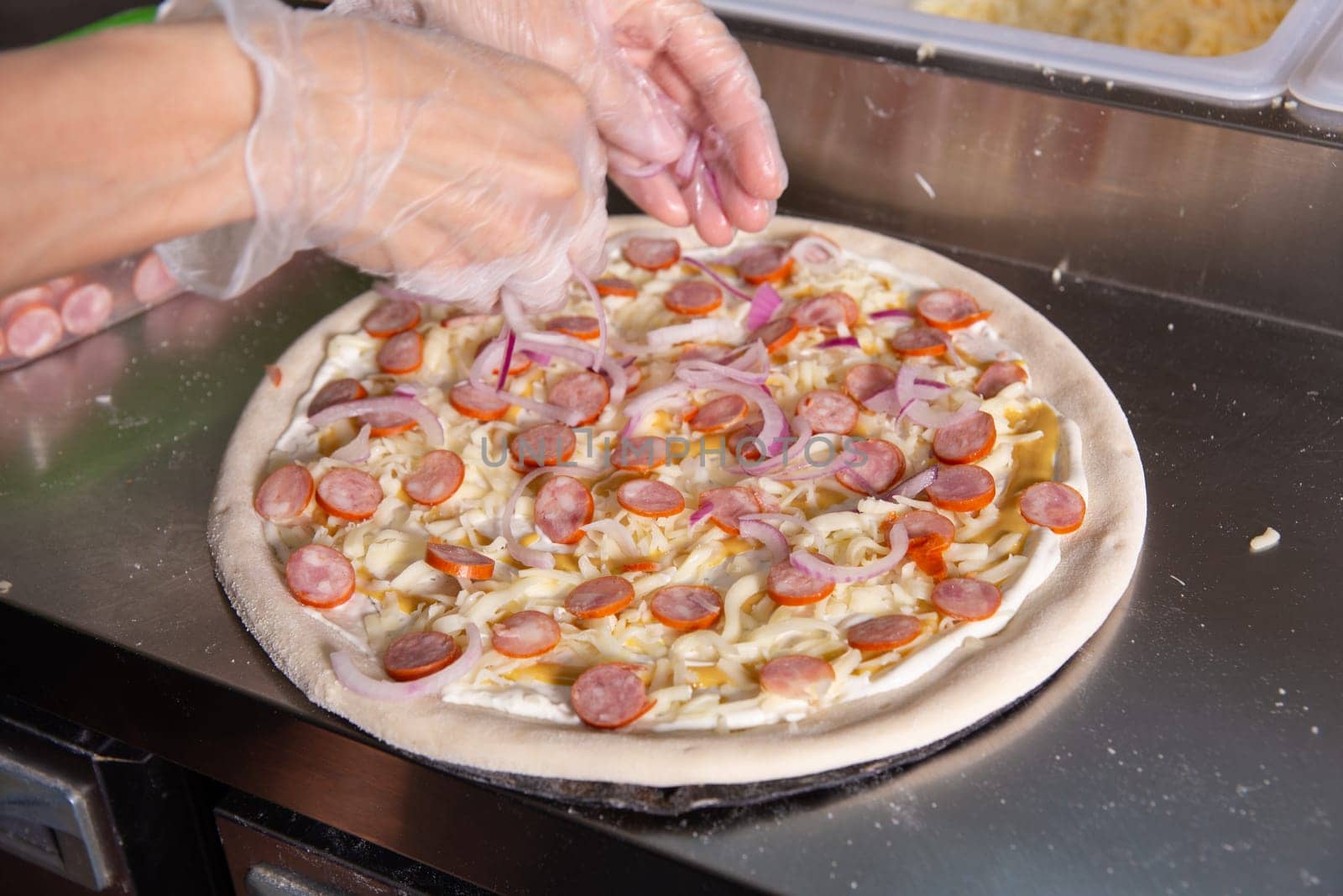 The chef prepares a classic Italian pizza with sausages, mushrooms and tomatoes. The cook sprinkles the pizza with chopped onions