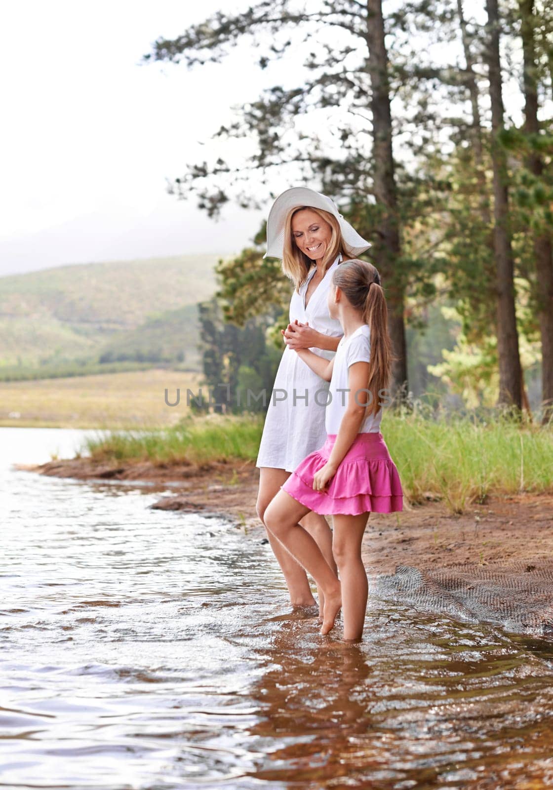 Mother, daughter and happiness outdoor in river for bonding, support or holding hands on holiday in nature. Family, woman and girl child with smile or adventure on vacation, travel and lake with love by YuriArcurs