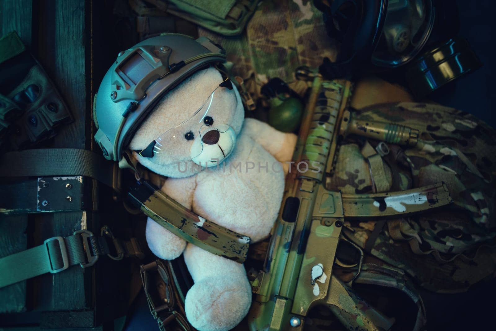 teddy bear in a military helmet among a pile of military ammunition, a rifle, grenades, a bulletproof vest, a helmet and other tactical airsoft items