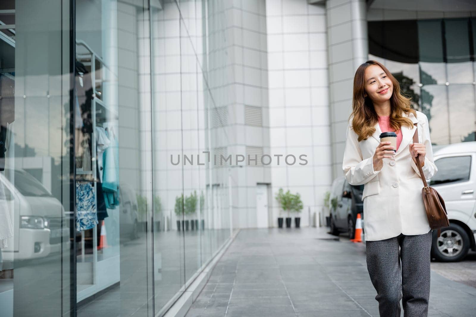 A woman uses her phone to stay connected while drinking coffee outside her office building. She is a modern business professional.