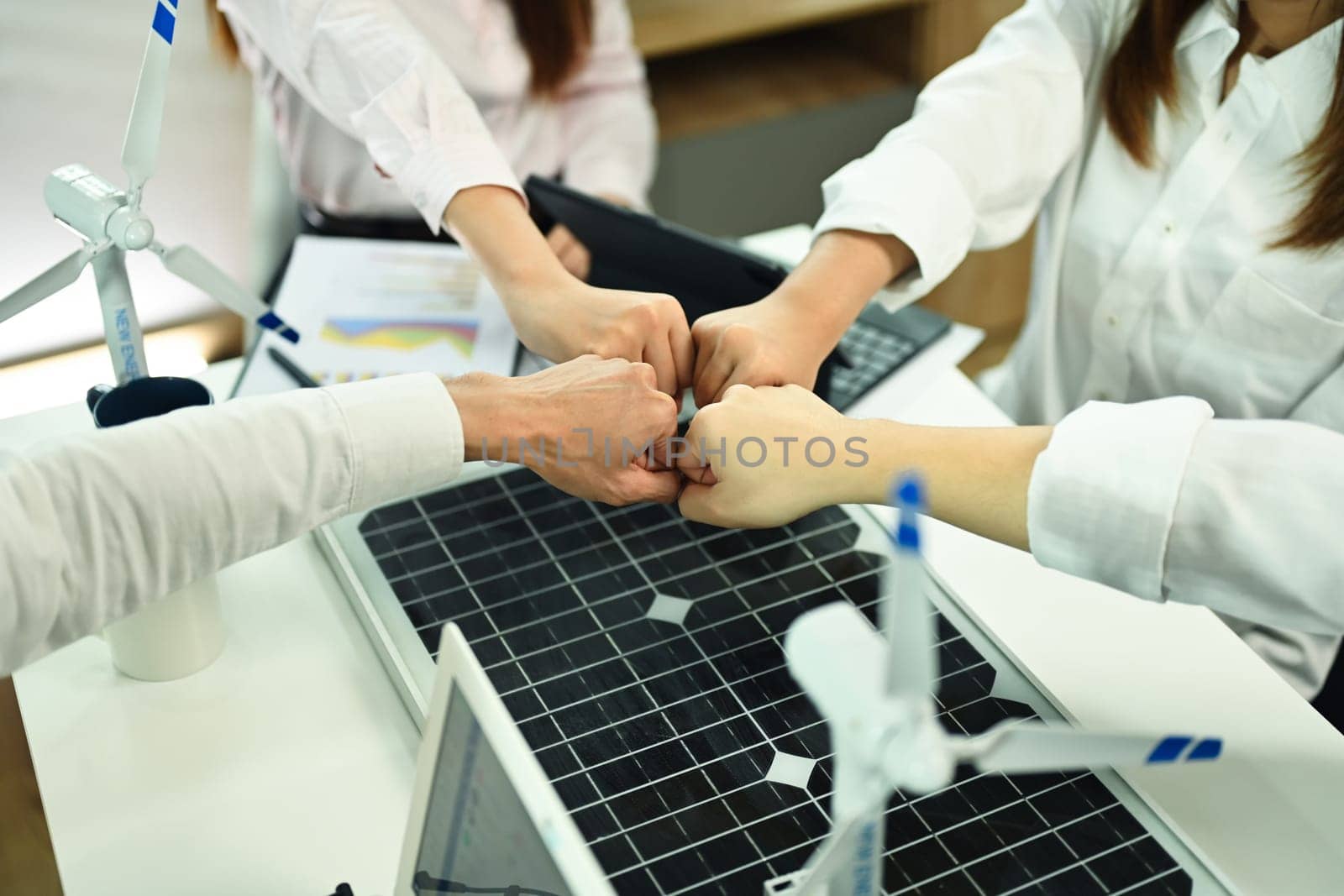 Team of alternative energy engineers join hand together over meeting table.