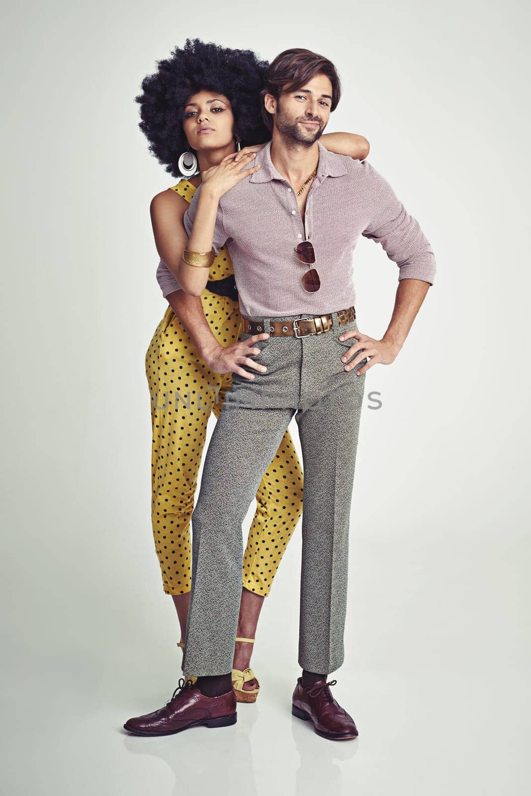 Couple, portrait and fashion in confidence for style, outfit or clothing on a gray studio background. Young interracial man and woman in stylish retro or vintage pants, shirt or jumpsuit with jewelry by YuriArcurs