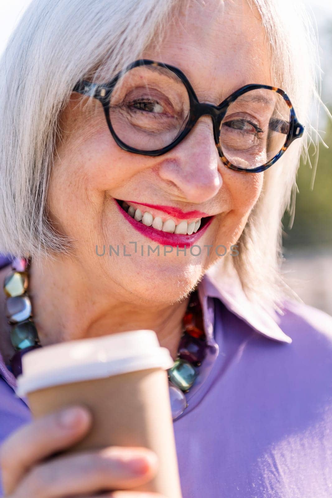 close up portrait of a beautiful senior woman smiling looking at camera with a takeaway coffee, concept of elderly people leisure and active lifestyle, copy space for text